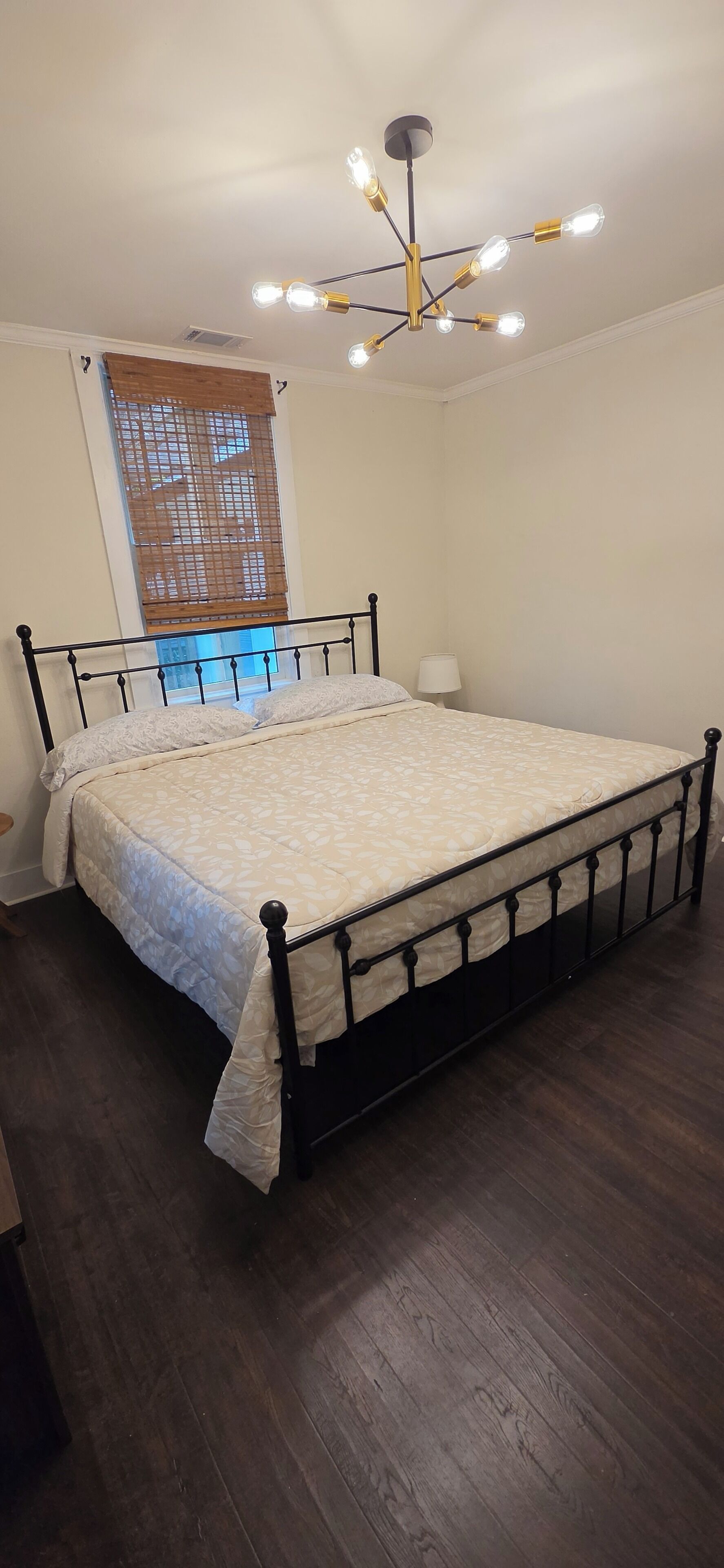 Een slaapkamer met een bed, een plafondlamp, een raam met zonwering en een nachtkastje.