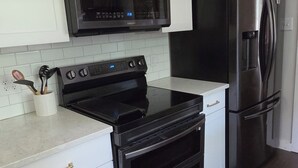 Een keuken met witte kastjes, een zwarte magnetron, een zwart fornuis, een zwarte oven en een zwarte koelkast.