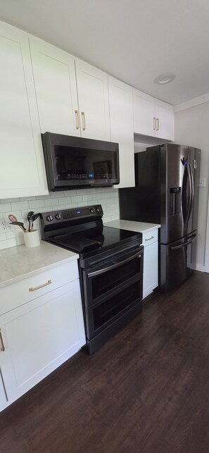 A kitchen with white cabinets, a black microwave, a black stove, a black oven, and a black refrigerator.