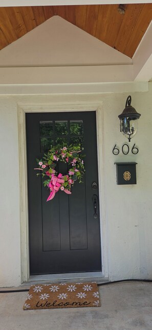 A black door with a pink floral wreath, a mailbox with the number 606, and a welcome mat.