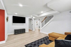 Ein modernes Wohnzimmer mit Flachbildfernseher, Holzboden, Treppe und einer Couch.