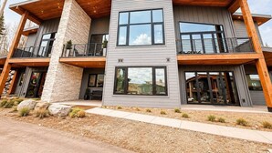 Una moderna casa a due piani con facciata in pietra, ampie finestre e un patio in legno.