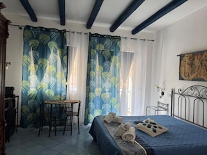 Ein Zimmer mit einem Bett, einem kleinen Tisch mit Stühlen und Vorhängen mit Blattmuster.