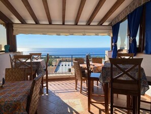 Una terraza con mobiliario de madera, vista al mar y un mantel estampado.