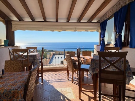 A terrace with wooden furniture, a view of the sea, and a patterned tablecloth.. Hellas