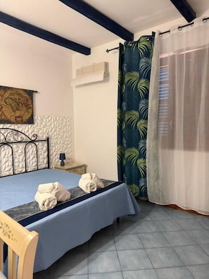 A bedroom with a bed, a chair, a map on the wall, and a curtain with a leaf pattern.