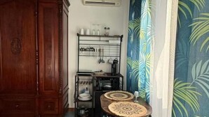 A room with a wooden cabinet, a small table with chairs, a metal rack with kitchen items, and a patterned curtain. - Hellas  (Macari)