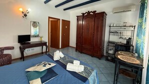 A room with a bed, a wooden wardrobe, a desk with a television, and a dining area with a table and chairs. - Hellas  (Macari)