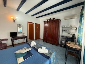 A room with a bed, a wooden wardrobe, a desk with a television, and a dining area with a table and chairs.