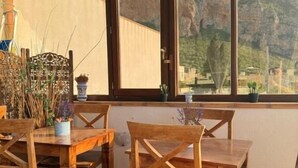 A wooden dining table with chairs, a window with a view of mountains, and a decorative plant arrangement. - Hellas  (Macari)