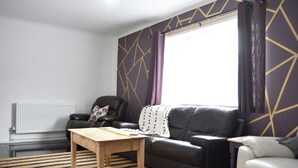 A living room with a sofa, a table, a radiator, and a window with curtains.