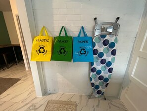 Eine Wand mit drei Recyclingbeuteln, beschriftet mit 'PLASTIC', 'GLASS' und 'PAPER', die an Haken hängen.