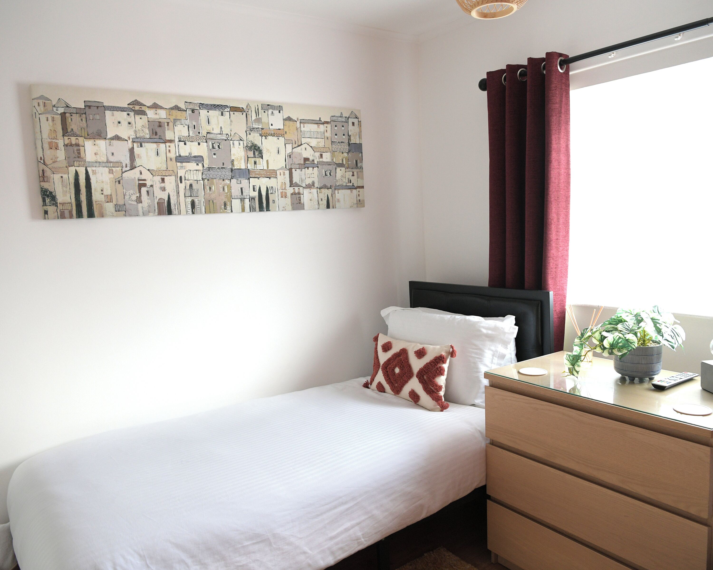 Un dormitorio con cama, cómoda, ventana con cortinas y una obra de arte en la pared.