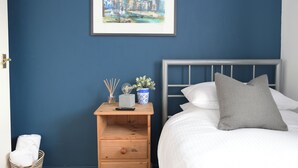 A bedroom with a bed, a nightstand, a framed painting, a basket, and a wooden dresser.