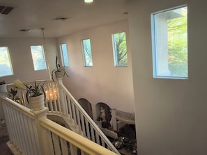 A staircase with white railings, potted plants, and a view of trees through windows.