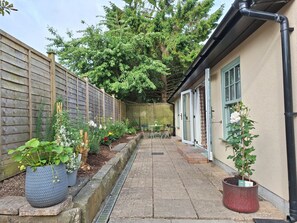A narrow pathway leading to a building with a green door, surrounded by a wooden fence and various potted plants. - Cosy Garden Cottage, Combe Down | Free Parking (Bath and North East Somerset)