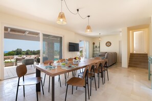 A spacious dining area with a long table, multiple chairs, and pendant lighting. - High-end pool villa on 2 levels with sea view (Torre Pali)