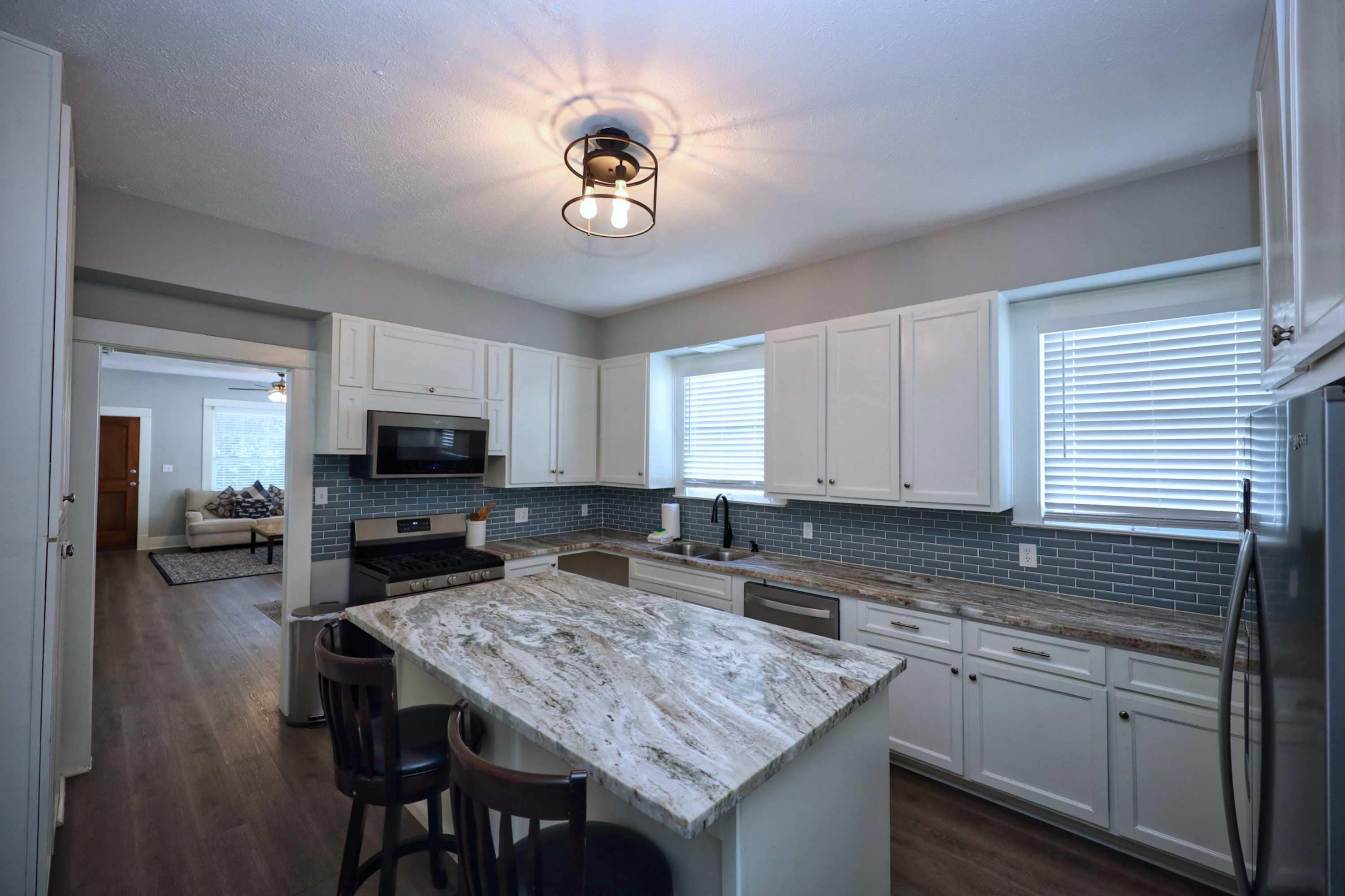 A modern kitchen with white cabinets, a granite island, stainless steel appliances, and a ceiling light fixture.