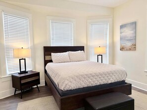 A bedroom with a bed, two bedside tables with lamps, a bench, and a painting on the wall. - Uptown Cottage Near Downtown (Galveston)