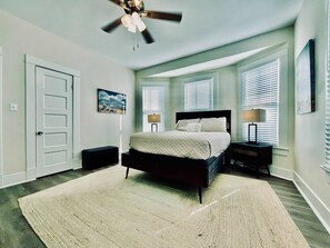 Ein Schlafzimmer mit Bett, Deckenventilator, Nachttisch, Lampe und einem Fenster mit Jalousien.