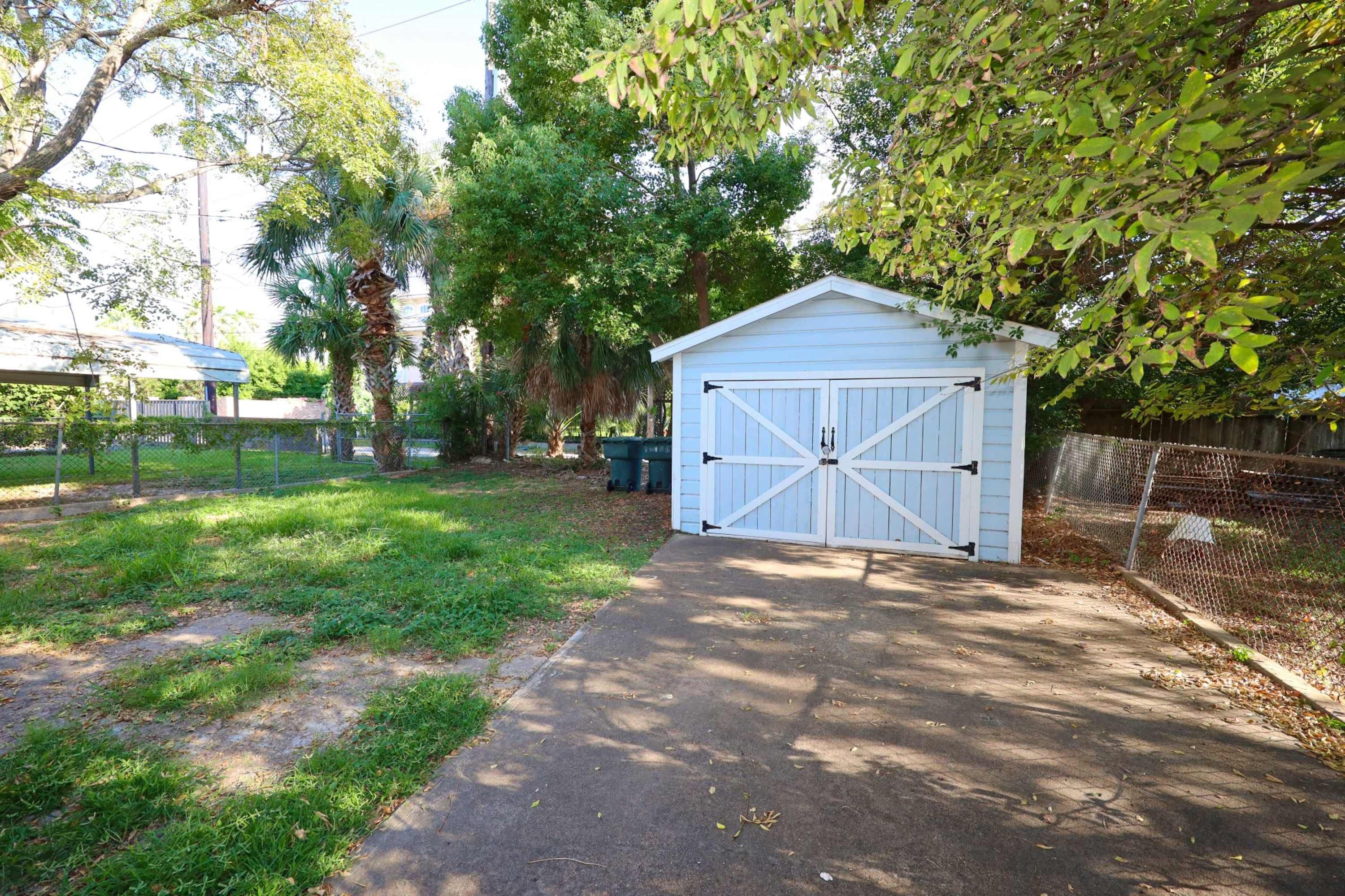 A covered garage with a metal gate, surrounded by a chain-link fence, and a grassy area with trees.
