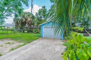 A blue garage with a concrete driveway, surrounded by greenery and a fence. - Uptown Cottage Near Downtown (Galveston)
