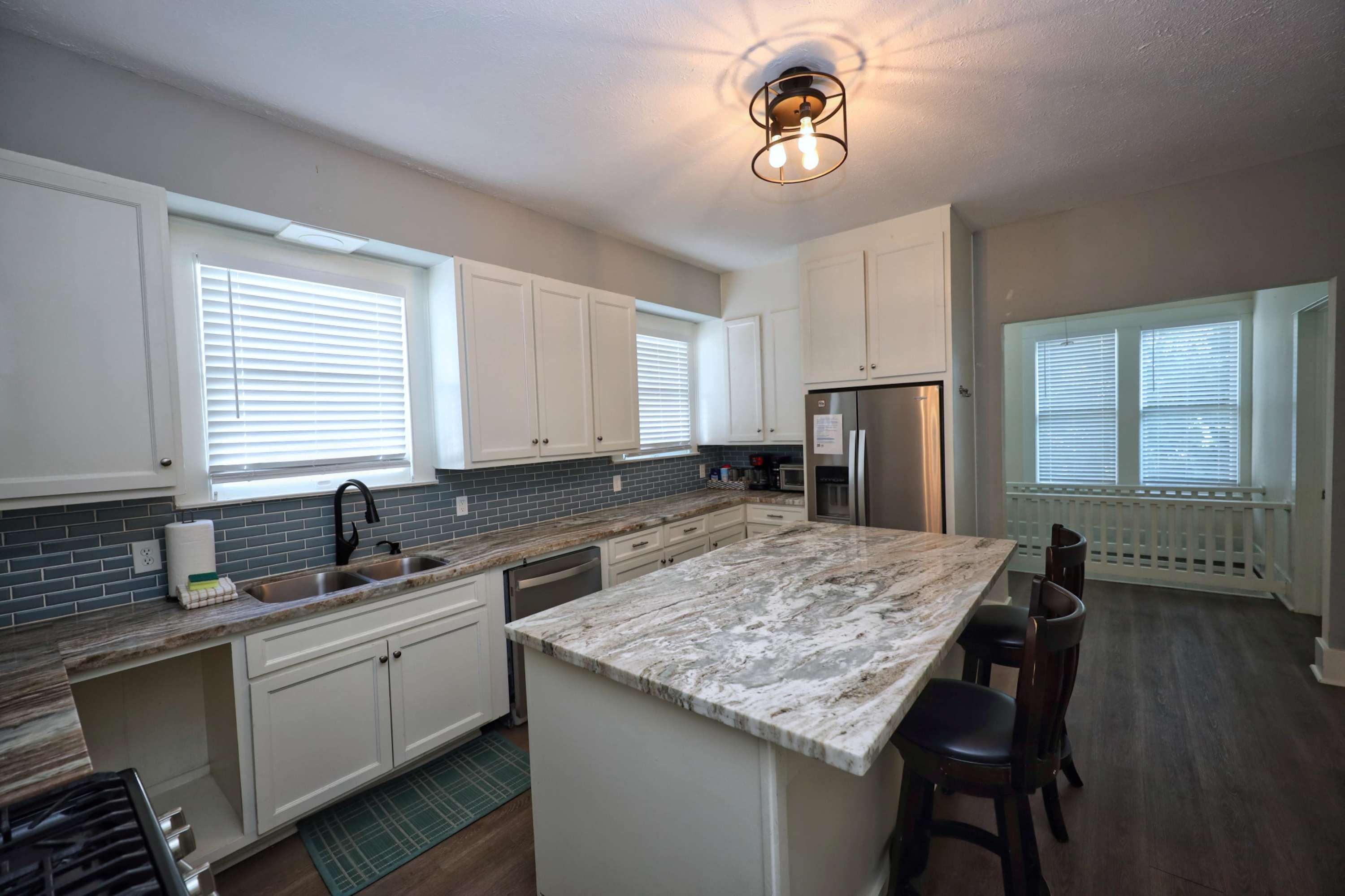 A modern kitchen with white cabinets, a marble countertop, and a built-in island with bar stools.
