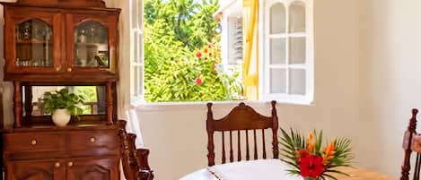 A room with a dining table, a wooden cabinet with glass doors, and a window with an open view of greenery.