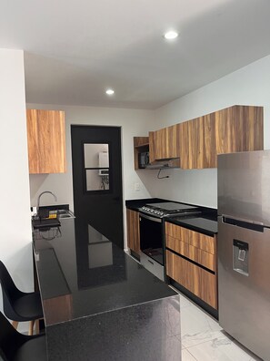 Eine moderne Küche mit schwarzer Arbeitsplatte, Holzschränken, einem Edelstahlkühlschrank und einem eingebauten Backofen.