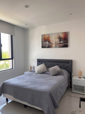 A modern bedroom with a large bed, two bedside tables, a nightstand, and a painting on the wall. - Apartment near the airport with pool and office all inclusive (Cancún)