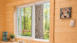 L’intérieur d’une cabane en bois comprend un comptoir de cuisine, deux tabourets de bar, une fenêtre donnant sur les arbres et un tableau accroché au mur.