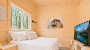 Une chambre à coucher dans un chalet en bois, avec un lit, une table de chevet, un téléviseur et un tableau représentant un cheval.