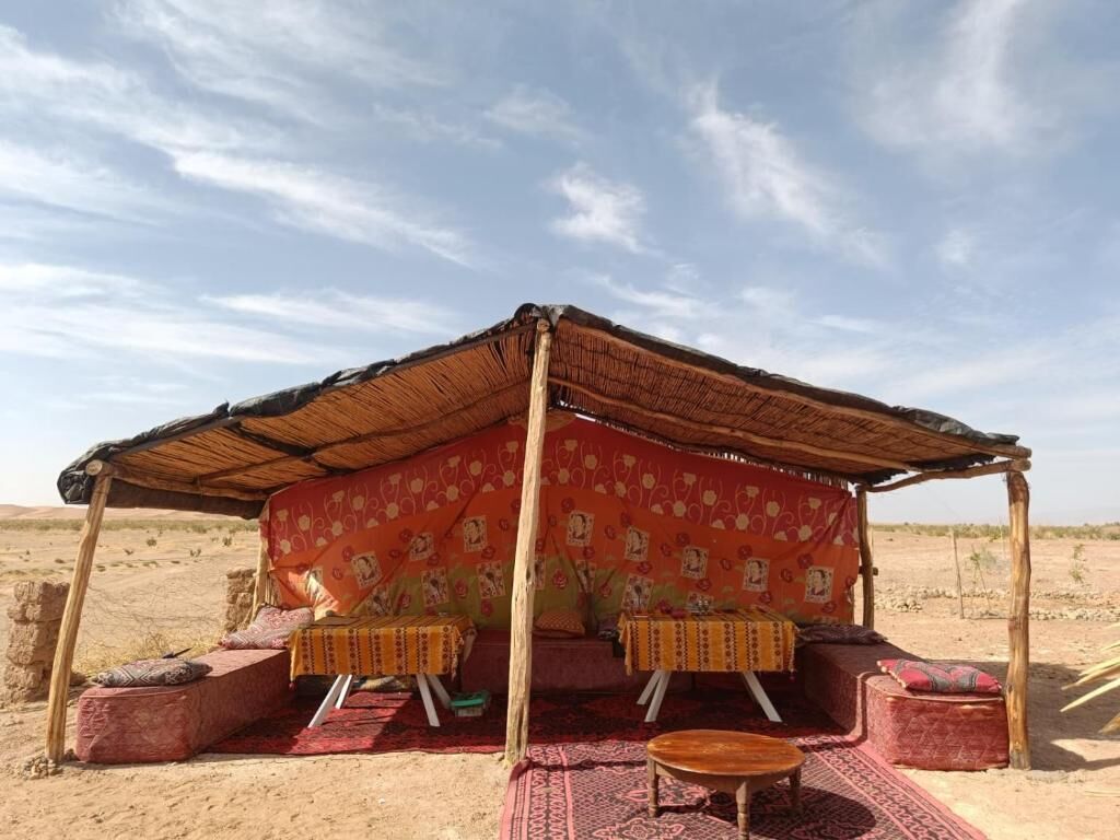 A traditional tent with a patterned fabric interior, wooden furniture, and a sandy landscape.