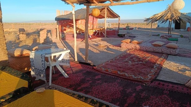 Un espacio de descanso al aire libre rústico con techo de paja, una mesa pequeña y alfombras de colores.