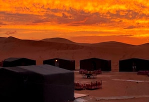 A desert landscape with multiple tents and a table set for dining, suggesting a campsite or temporary accommodation. - Desert Erg Chigaga (M'Hamid El Ghizlane)