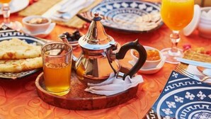 Un desayuno tradicional marroquí con un hervidor de té, vasos de zumo de naranja y una variedad de pasteles sobre un mantel estampado.