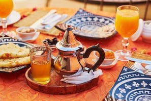 A traditional Moroccan breakfast setting with a teapot, glasses of orange juice, and a variety of pastries on a patterned tablecloth. - Desert Erg Chigaga (M'Hamid El Ghizlane)