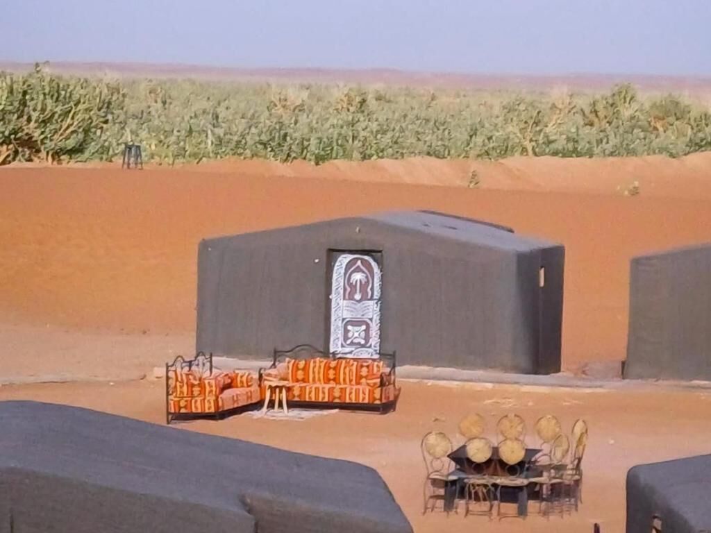 A desert landscape with a building featuring a large door and a small table with chairs.