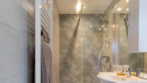 Een moderne badkamer met een douchecabine van glas, een witte wastafel en een houten vloer.