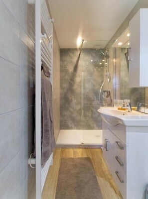 Ein modernes Badezimmer mit einer Duschkabine aus Glas, einem weißen Waschbecken und einem Holzboden.