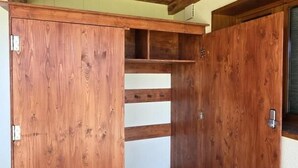 Een kamer met een stenen vloer, houten balken in het plafond en een ingebouwde houten garderobe met schuifdeur.