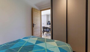 Ein Schlafzimmer mit einem Bett, einer Holztür und Blick in einen Essbereich.