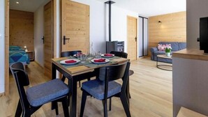 Een moderne eethoek met een houten tafel voor vier personen, twee blauwe stoelen, en een klein keukenhoekje met een fornuis en een spoelbak.