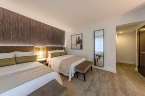 Quarto de hotel com duas camas, um banco, uma luminária fixada na parede e um quadro emoldurado.