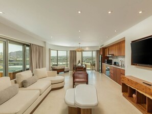A spacious living area with a sofa, a dining table, and a kitchen with wooden cabinets and a flat-screen TV. - Luxury 3BR Suite at Corazón Cabo Resort & Spa  Ocean Views & Rooftop Pool (Cabo San Lucas)