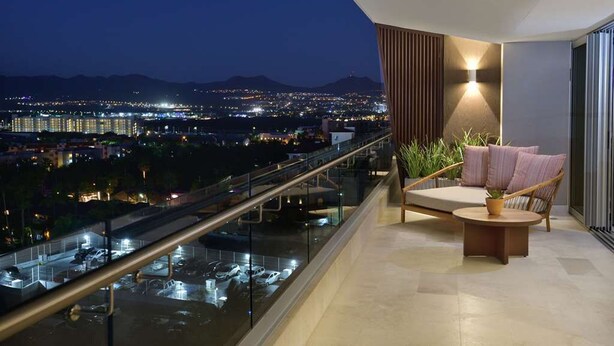 Ein Balkon mit Blick auf eine nächtliche Stadtlandschaft, eine gepolsterte Sitzecke und ein Blumentopf.
