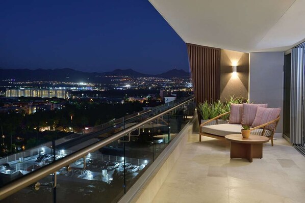 A balcony with a view of a cityscape at night, a cushioned seating area, and a potted plant. - Luxury 3BR Suite at Corazón Cabo Resort & Spa  Ocean Views & Rooftop Pool (Cabo San Lucas)