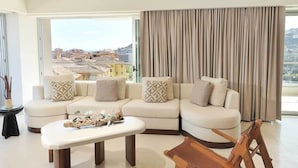 Ein modernes Wohnzimmer mit einem Ecksofa, einem Couchtisch und Blick auf eine Stadtlandschaft durch große Fenster.