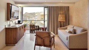 Ein modernes Hotelzimmer mit Balkon, einer Couch, einem Sessel, einem kleinen Tisch und einer Holzkabine mit Waschbecken.