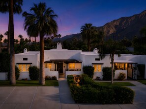 Un edificio blanco con patio, palmeras y montañas al fondo.